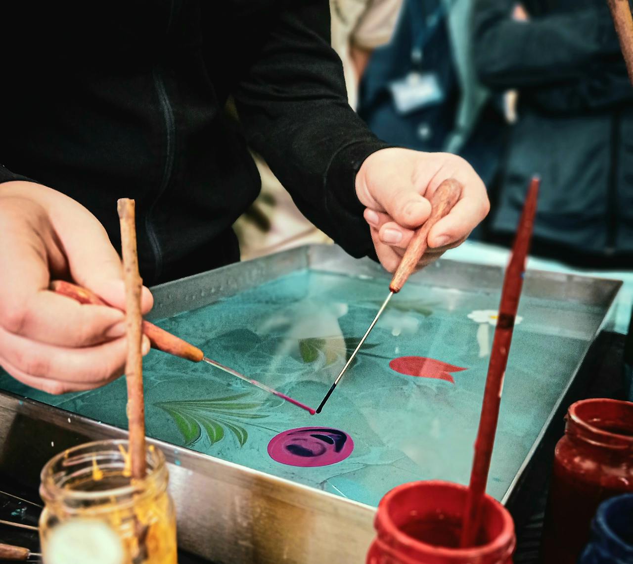 Artist demonstrating Ebru water marbling technique in Siirt, Türkiye using traditional tools and vibrant colors.